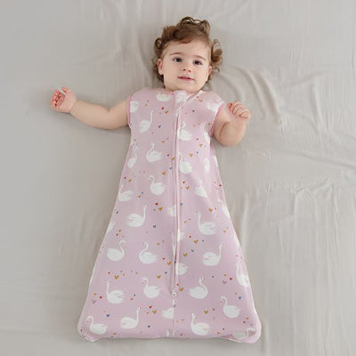 Allongée sur le lit, la fillette porte une gigoteuse bébé rose ornée de cygnes délicats.