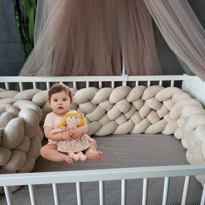 Assise avec sa poupée, la fillette repose dans un lit blanc borde d'un tour de lit tressé beige