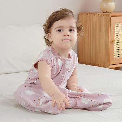Assise sur le lit, la fillette porte une gigoteuse bébé rose ornée de cygnes.