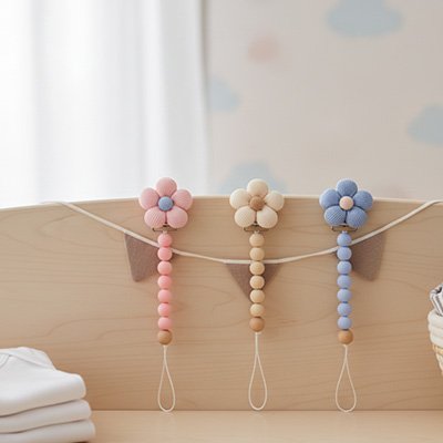 Attaché tetine : son design floral se décline en trois coloris tendres rose poudré, beige naturel et bleu pastel.