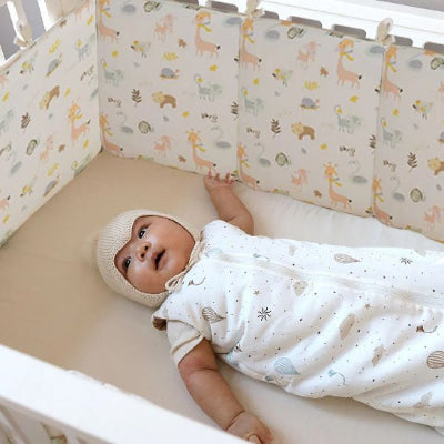 Autour du lit où bébé est allongé, un tour de lit bebe rembourré aux motifs d’animaux de la forêt apporte confort et sécurité.