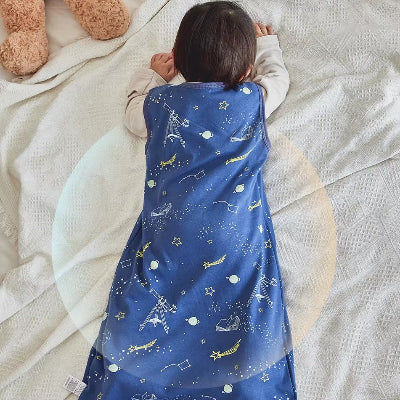 Bébé allongé dans une gigoteuse turbulette bleue décorée de motifs spatiaux.