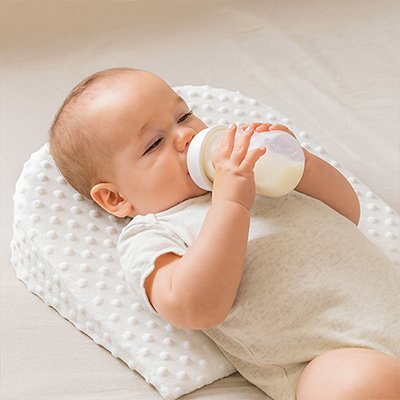 Bébé allongé dans son lit, sur le dos, buvant son biberon sur un plan incliné bébé Anti-Reflux 15° DreamerBaby™ blanc