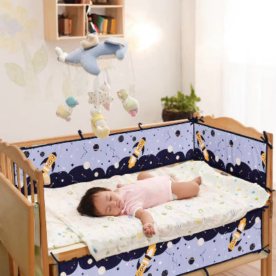 Bébé dort paisiblement dans son lit entoure d'un tour de lit bebe garcon décoré d'un motif spatial avec fusées, étoiles, constellations et planètes