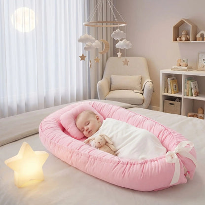  Bébé emmailloté et endormi dans son reducteur de lit bebe SlaapNestje™ rose, posé sur le grand lit. 