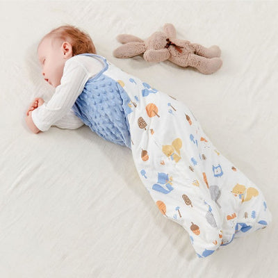 Bébé endormi sur un lit, vêtu d’une turbulette hiver, bleue matelassée en haut et blanche avec des motifs d’animaux en bas et dans le dos