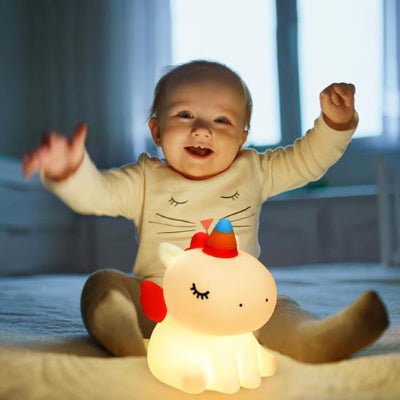 Bébé joue paisiblement devant sa bébé veilleuse UniLight™ en  forme de licorne, sous sa douce lumière