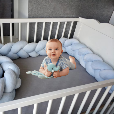 Bébé profite d'un moment doux sur le ventre avec son doudou dans un lit sécurisé par un tour de lit tresse bleu pastel