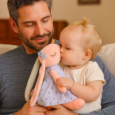 Dans les bras de son papa, la fillette embrasse tendrement son doudou lapin, pendant que papa sourit de bonheur.