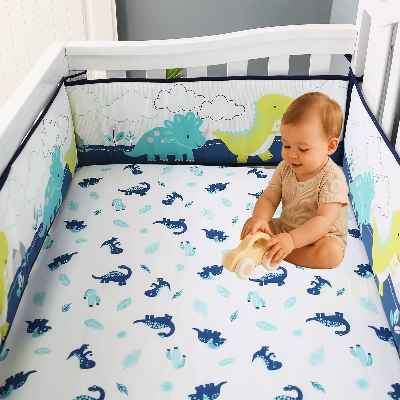 Dans son lit décoré d'un tour de lit bebe garcon aux dinosaures, un garçon s'amuse avec sa voiture en bois.