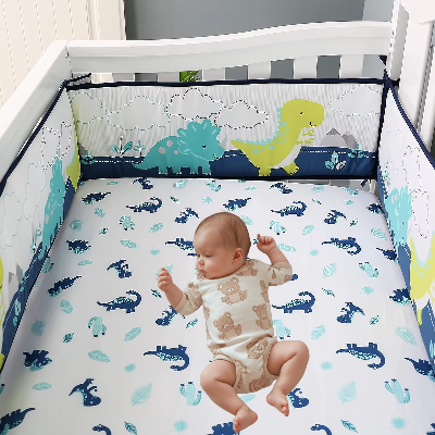 Dans son lit entoure d'un tour de lit bebe garcon dinosaures colores, un bébé allonge observe avec curiosité les motifs de dinosaures bleus sur le drap blanc.
