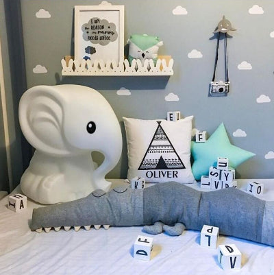 Dépose parmi les cubes à lettres le tour de lit pour bebe fait face à un éléphant blanc et a un mur décoré de nuages