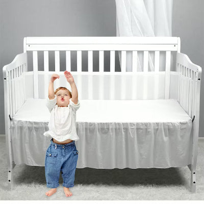 Devant son lit, l'enfant lève joyeusement les mains tandis que le tour de lit respirant blanc forme autour de son lit un cocon lumineux et rassurant.