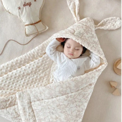 Endormi sur un lit blanc, le bébé est confortablement emmitouflé dans sa turbulette décorée d’une forêt fantastique