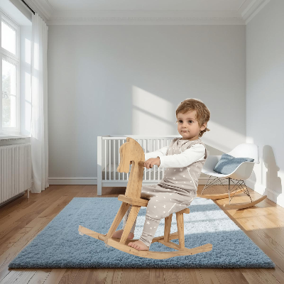 Enfant est assis sur un cheval à bascule en bois, vêtu d’une gigoteuse beige à motifs étoiles