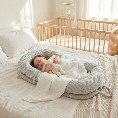  Enfant endormi dans son reducteur de lit bebe WeedgePood™ gris déposé sur le lit des parents, son doudou dans ses bras.