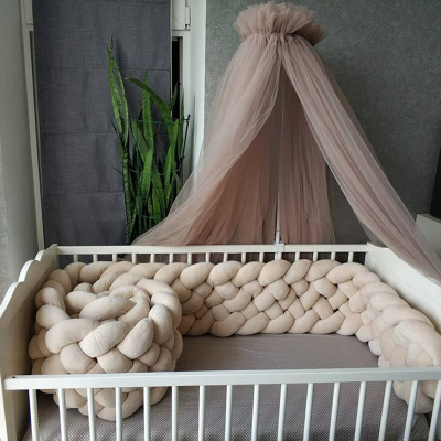 Entoure d'un tour de lit tressé beige, le lit bébé blanc sous son ciel de lit rose poudre offre un cocon doux et harmonieux