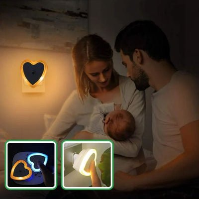 Maman fait dormir son bébé dans ses bras pendant que le papa le regarde dormir paisiblement sous la lumière de sa veilleuse murale bebe DreamNight™ en forme de cœur.