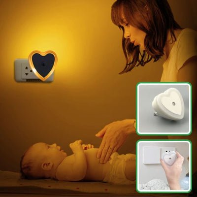 Maman fait un massage du ventre à son bébé, sous la lumière de sa veilleuse murale bebe DreamNight™ en forme de cœur.