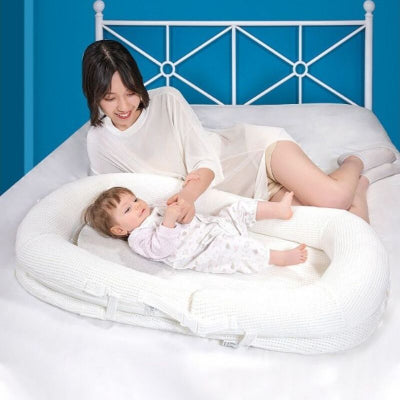 Maman installée dans son lit et joue avec son bébé qui est dans son reducteur de lit bebe WeedgePood™ blanc