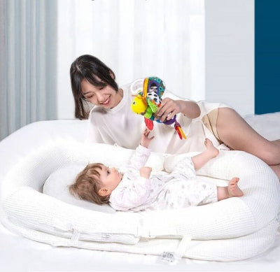  Maman joue avec son bébé installé dans son reducteur de lit bebe WeedgePood™ blanc, sur son lit.