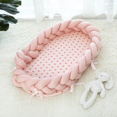 Reducteur de lit pour bebe SweetSnug™ rose posé sur un tapis, accompagné de son doudou lapin sur le côté