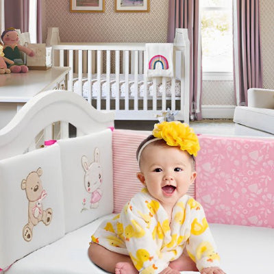 Souriante, la fillette est assise dans son lit, protégée par son tour de lit bébé.