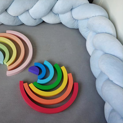 Tour de lit tresse bleu pastel sur le lit avec deux arcs-en-ciel en bois au centre pour un espace doux et chaleureux