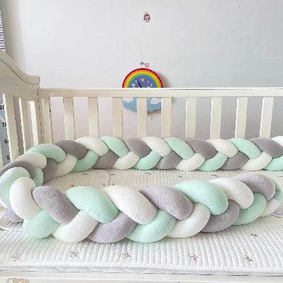 Tresse tour de lit aux tons gris, blanc et vert disposée dans un lit bébé blanc