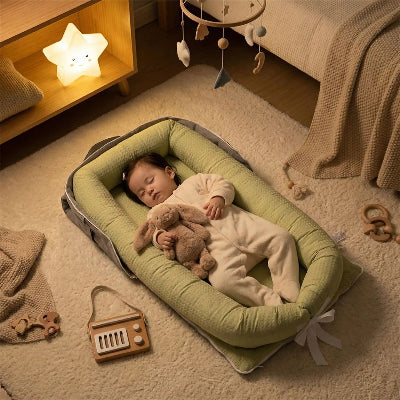 Une fillette endormie dans son réducteur de lit bébé DreamyPood™ vert, son doudou dans les bras, est déposée sur le tapis à côté du lit, sous la lumière de la veilleuse