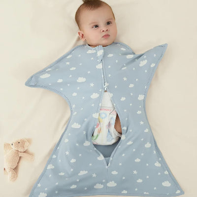 Un bébé est allongé calmement sur un lit, enveloppé dans une turbulette gigoteuse bleue aux motifs de nuages et d’étoiles
