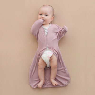 Un bébé allongé sur le lit, vêtu d’une gigoteuse emmaillotage violette, avec les pieds dépassant librement à l’extérieur