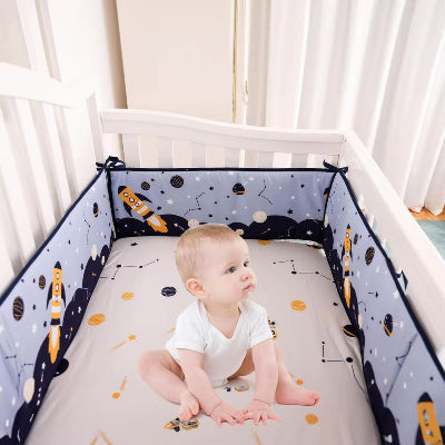 Un bébé est assis dans son lit entoure d'un tour de lit bebe garcon décoré de motifs spatiaux comprenant des fusées, des étoiles, des constellations et des planètes.