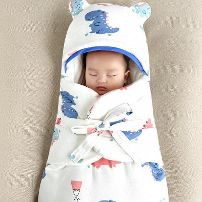 Un bébé dort paisiblement, emmailloté dans une gitoteuse hiver bebe blanc à motifs de petits dinosaures, avec une capuche aux oreilles adorables
