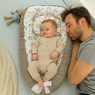 Bébé endormi dans son réducteur de lit bébé, le papa dort sur le côté
