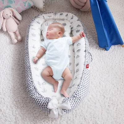 Un bébé endormi paisiblement dans son Berceau Bébé NidPortableBébé™ Couronne, déposé sur le tapis, avec son doudou lapinou à ses côtés.