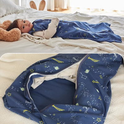 Un bébé est allongé sur le lit, dans une gigoteuse turbulette bleue décorée de motifs spatiaux