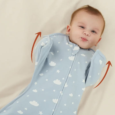 Un bébé est allongé sur un lit, enveloppé dans une turbulette gigoteuse bleue ornée de motifs de nuages et d’étoiles.