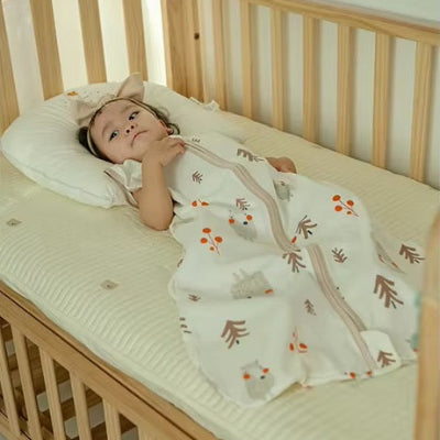 Un bébé est confortablement installé dans une gigoteuse turbulette blanche décorée de jolis ours.