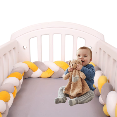 Un bébé joyeux, doudou en main, assis dans son lit protégé par une tresse de lit 4 m jaune, blanche et grise.
