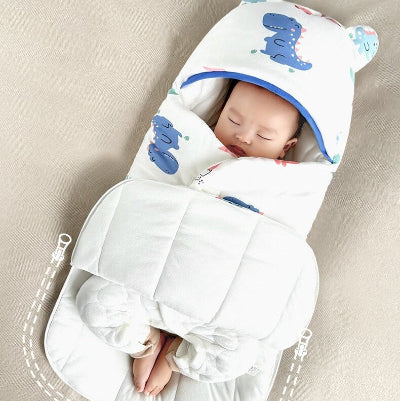Un bébé profondément endormi est emmailloté dans une gigoteuse hiver bebe blanche décorée de dinosaures et d’une capuche craquante.