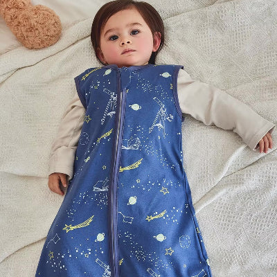 Un bébé repose paisiblement, enveloppé dans une gigoteuse turbulette bleue aux motifs de l’espace.