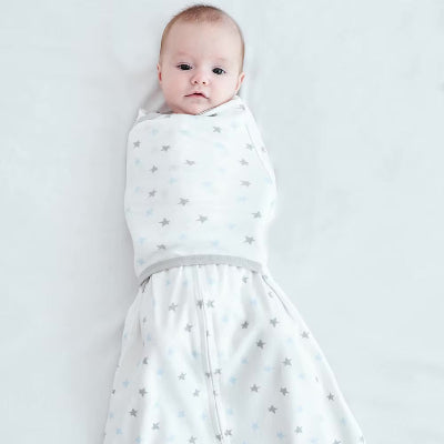 Un bébé repose sur un lit blanc, délicatement enveloppé dans une gigoteuse emmaillotage douce aux motifs d’étoiles.