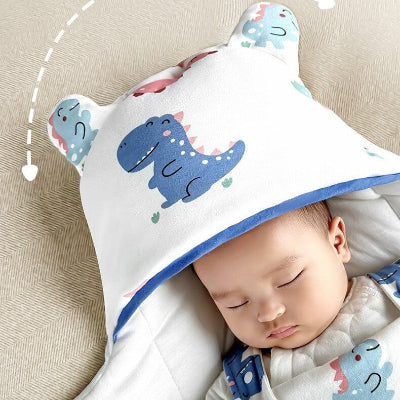 Un bébé paisible sommeille, bien au chaud dans une gigoteuse hiver bebe blanche aux motifs de dinosaures, complétée par une capuche à oreilles adorables