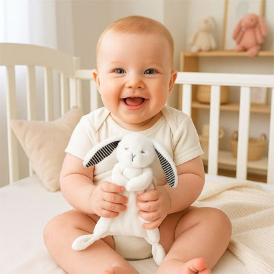 Bébé souriant assit dans son lit, son doudou lapin ses mains