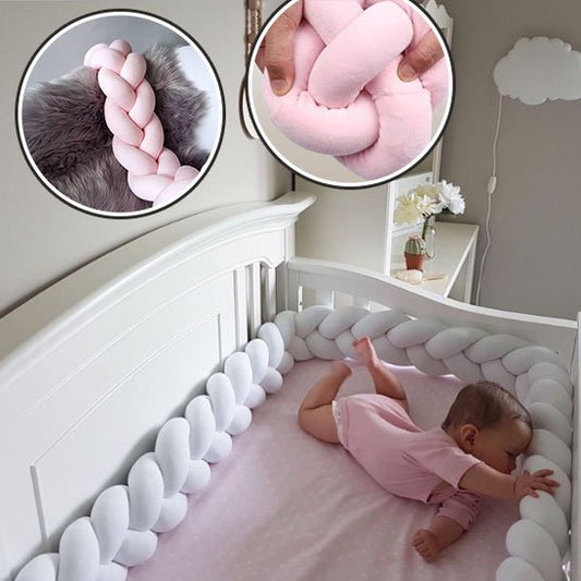Bébé sur son ventre joue avec le tour de lit tressé