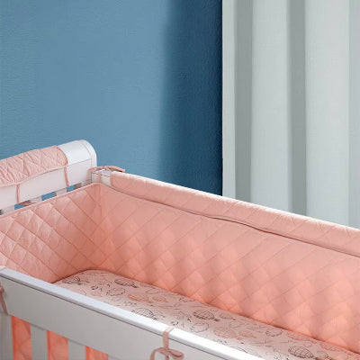 Un cocon rose enveloppe le lit de bébé grâce à un tour de lit bébé fille matelasse créant une atmosphère tendre et chaleureuse.