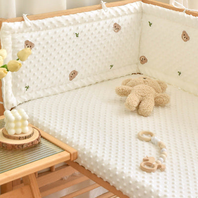 Un doudou ours est posé sur le lit du bébé, entouré d’un tour de lit bébé blanc décoré de petites têtes d’oursons.