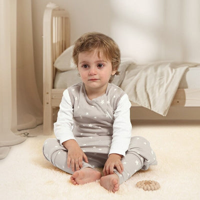Un enfant est assis sur un tapis dans sa chambre, vêtu d’une gigoteuse beige parsemée d’étoiles.