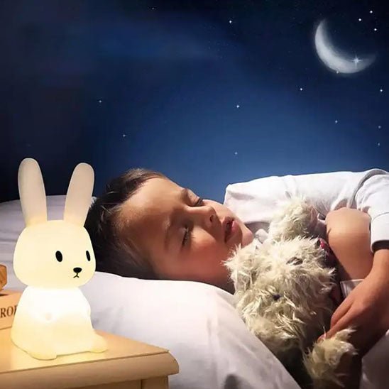 Un enfant endormi paisiblement, tenant son doudou dans ses bras sous la lumière de sa veilleuse bébé Glowbit™ en forme de lapin